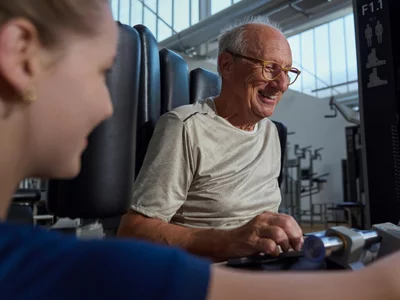 Ein motivierter älterer Herr beim begleiteten Training bei Kieser – unterstützt durch eine professionelle Instruktorin für sicheres Krafttraining.