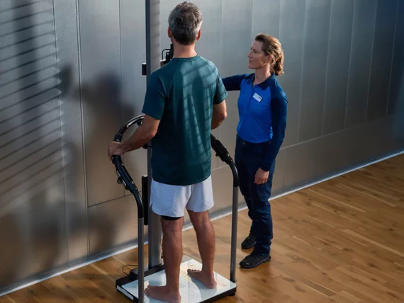 Ein Kunde führt unter Anleitung einer Instruktorin eine professionelle BIA Messung bei Kieser durch, um seine exakte Körperzusammensetzung zu bestimmen.