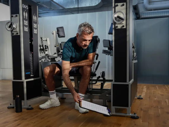 Trainierende Person stellt vor dem Training ein Krafttrainingsgerät in einem Kieser Studio ein. Im Hintergrund sind weitere Trainingsmaschinen zu sehen.