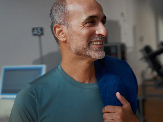 Homme dans une salle de sport après une séance de musculation, une serviette sur l'épaule, faisant des exercices du plancher pelvien pour améliorer sa stabilité et sa continence.