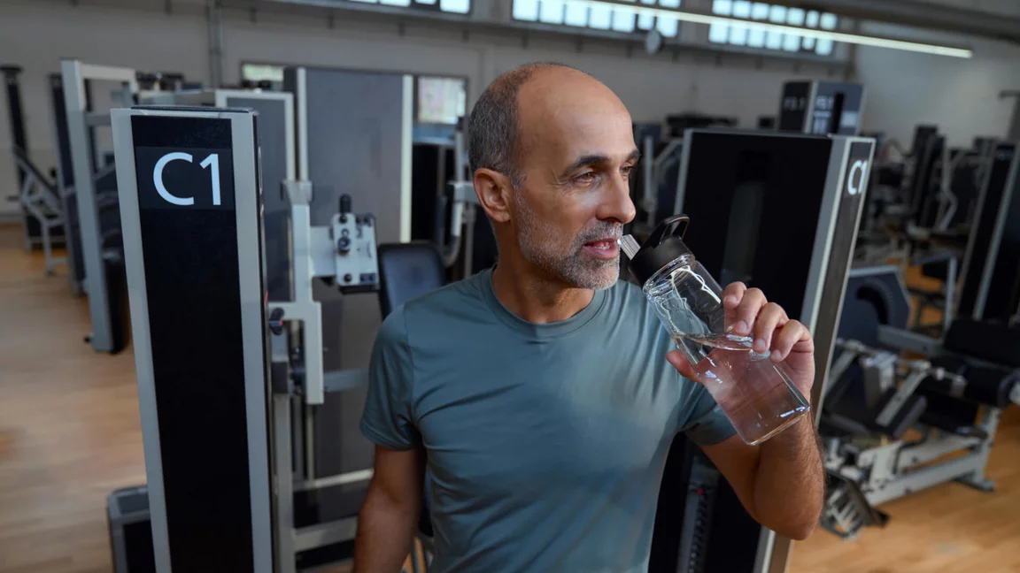 Ein Mann trinkt Wasser während einer Trainingspause im Kieser Studio zur Unterstützung der Regeneration.