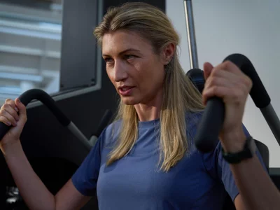 Femme concentrée s'entraînant sur une machine de musculation grise dans un studio lumineux.