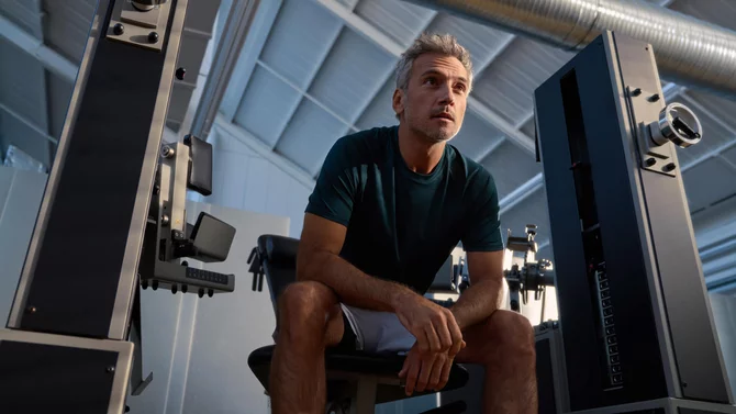 Homme concentré faisant de la musculation sur une machine grise dans une salle de sport moderne avec de hauts plafonds et un caractère industriel.