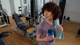 Eine zufriedene Kundin mit Handtuch und Wasserflasche nach dem Krafttraining im modernen Kieser Studio.