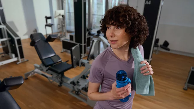 Eine zufriedene Kundin mit Handtuch und Wasserflasche nach dem Krafttraining im modernen Kieser Studio.