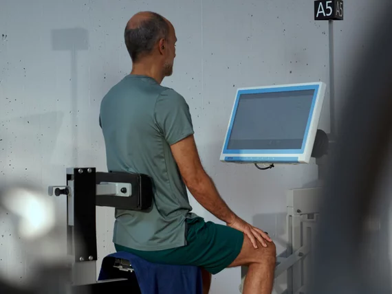 Un homme en position d'entraînement debout sur la machine A5 pour le plancher pelvien chez Kieser, concentré sur l'écran de biofeedback pour contrôler ses progrès.