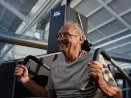 Ein älterer Mann mit Brille lacht bei einer kräftigenden Rückenübung an einer Trainingsmaschine zur Vorbeugung von Rückenschmerzen.