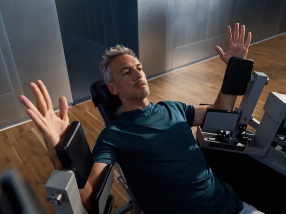 Une personne effectue un exercice sur un appareil de musculation. Les bras sont levés sur les côtés tandis que la personne s'entraîne sur un siège d'entraînement dans un studio Kieser.