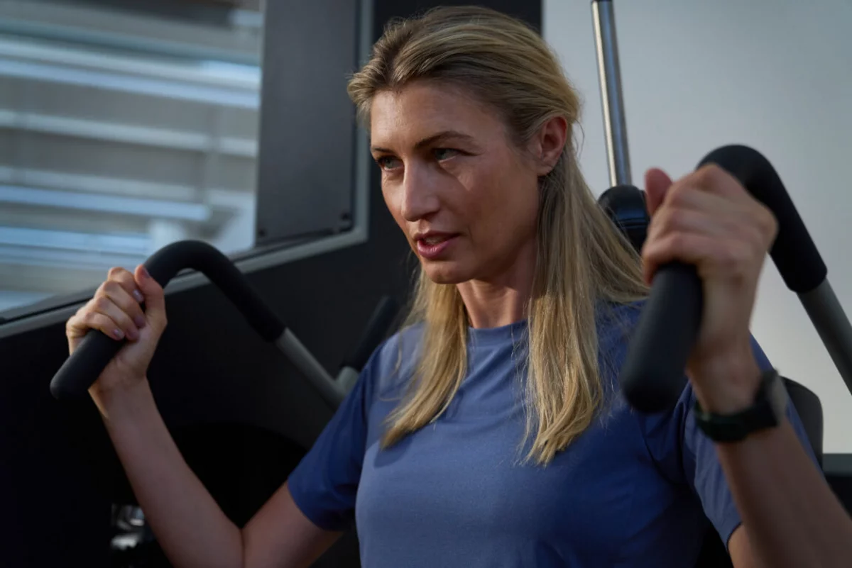 Porträtaufnahme einer konzentrierten Frau beim Training an einer Kraftmaschine, die Griffe fest umschlossen.