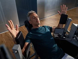 Mann bei einer Kraftübung zur Stabilisierung des Oberkörpers an einer grauen Trainingsmaschine auf Parkettboden.