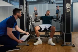Ein Trainierender an einer spezialisierten E4/5-Maschine erhält professionelle Begleitung durch einen Kieser Instruktor für korrektes Krafttraining.