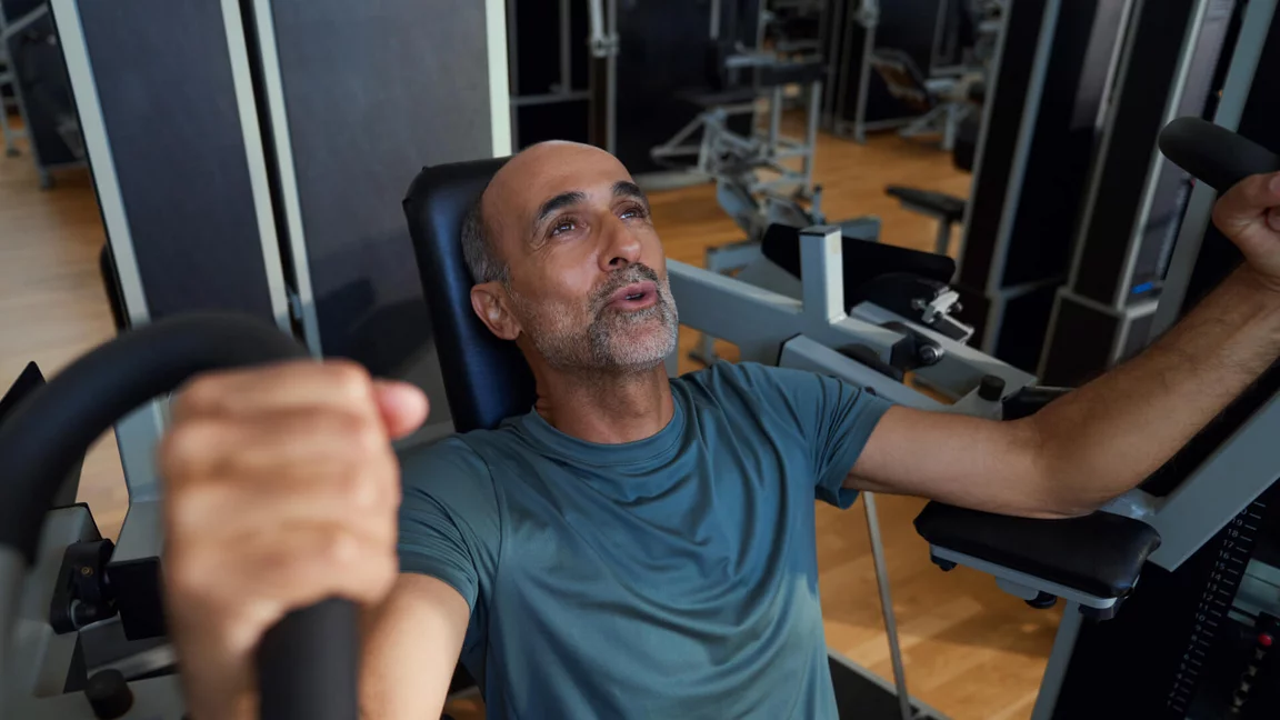 Une personne s'entraîne sur un appareil de musculation dans un studio Kieser. D'autres appareils d'entraînement sont visibles à l'arrière-plan.