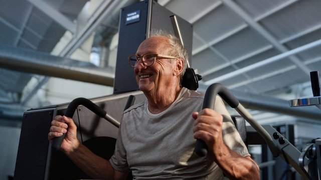 Ein lächelnder älterer Mann beim aktiven Rückentraining an einer Kieser-Maschine zur Vorbeugung von Rückenschmerzen.